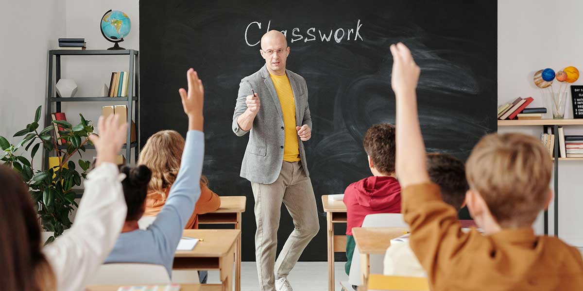 teacher in front of classroom with raised hands